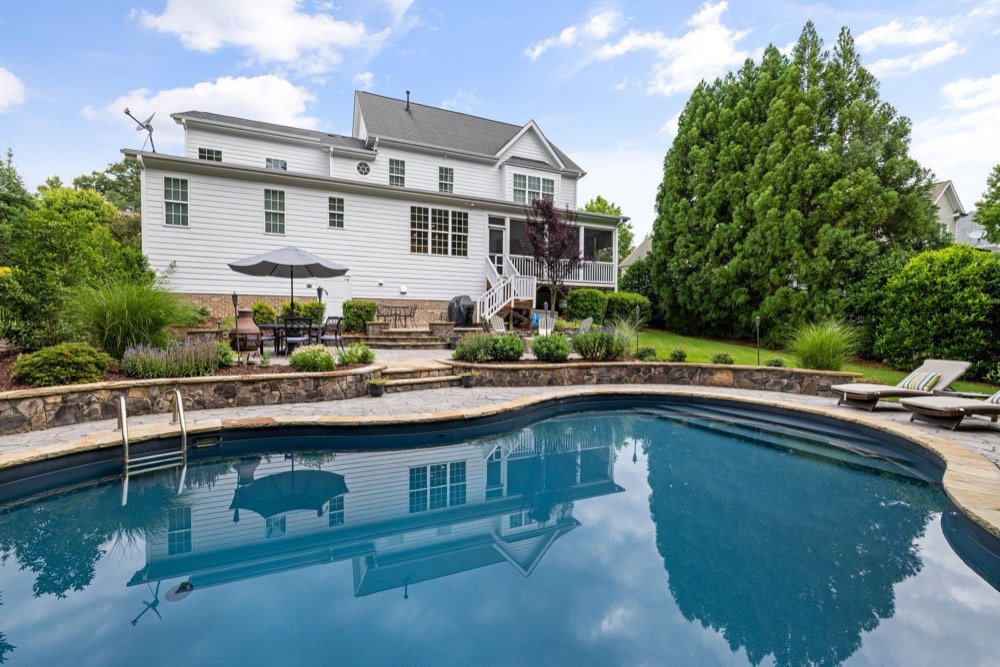 Backyard swimming pool and stone patio behind a home